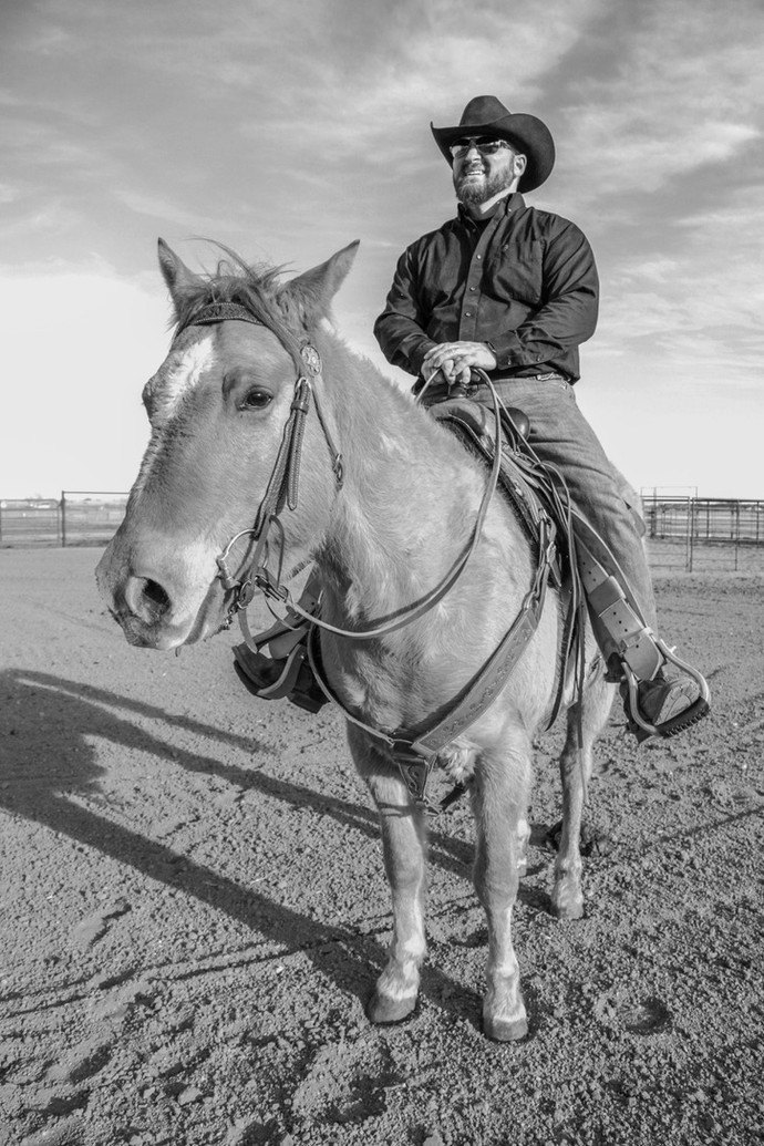 Josh Aragon on horseback in a black shirt and hat, in an arena under a big sky